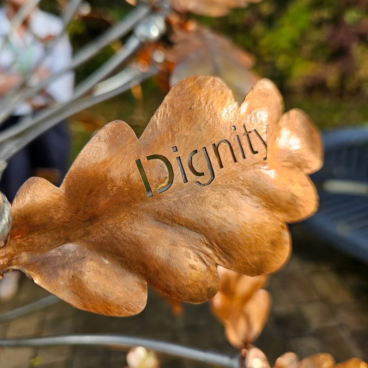 A copper oak leaf hanging on the tree with the word Dignity cut through it